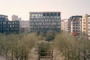 Ein Panoramablick auf den taz Neubau, im Vordergrund stehen die vielen Kastanienbäume des Kreuzberger Besselparks im noch zarten Grün