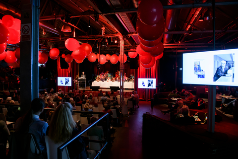 Das Bild zeigt die Genossenschaftsversammlung 2022 im Festsaal Kreuzberg. Es hängen Ballons von der Decke und der Raum ist rot ausgeleuchtet.