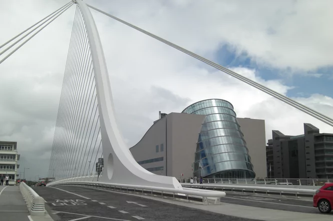 Im Vordergrund eine moderne Brücke, rechts ein zylindrisches Glasgebäude.