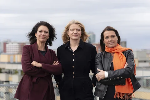 Die Chefinnenredaktion der taz, Ulrike Winkelmann, Katrin Gottschalk und Barbara Junge, stehen auf der Dachterasse des taz-Gebäudes, und schauen in die Kamera. Es windet und der Himmel ist bewölkt, sie tragen Übergangsjacken.