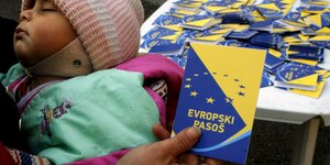 Eine Hand hält einen fiktiven europäischen Pass, daneben sieht man ein schlafendes Kind.