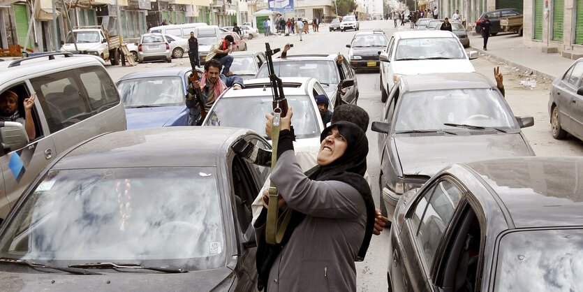 eine Frau hält zwischen Autos ein Gewehr in die Luft