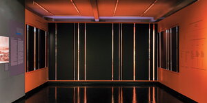 Eine mit schwarzem PVC verhängte Museumsvitrine in einem orangefarbenen Raum