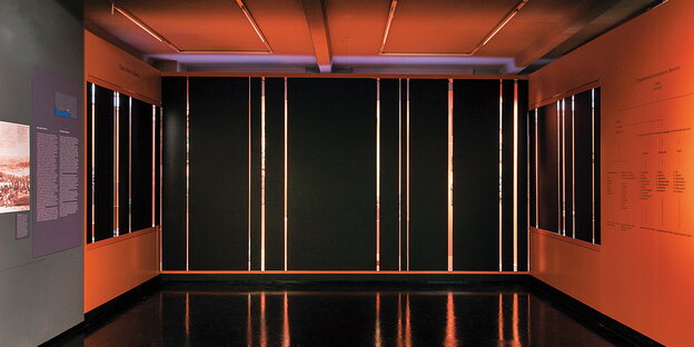 Eine mit schwarzem PVC verhängte Museumsvitrine in einem orangefarbenen Raum