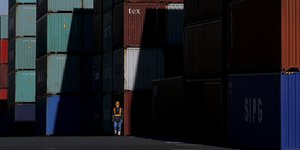 Ein Mensch mit Helm steht vor Containern im Hafen