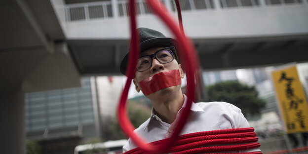 Ein Mann ist mit einem roten Seil gefesselt, vor ihm hängt eine rote Schlinge.
