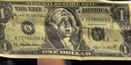 ein Dollarschein, auf dem George Washington die Hände über dem Kopf zusammenschlägt