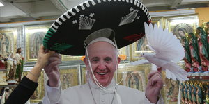 Eine Frau setzt dem Papst einen Mariachi-Hut auf. Er lacht in die Kamera und hält einen Spielzeugvogel in einer Hand