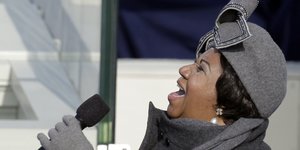 Aretha Franklin singt ins Mikro, trägt graue Mütze, Schal und Handschuhe