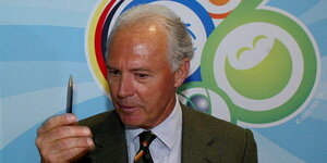 ein Mann hält einen Stift hoch, im Hintergrund das Logo der WM 2006