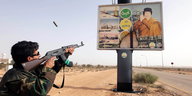 Ein Mann schießt auf eine Großanzeige auf der Gadaffi abgebildet ist