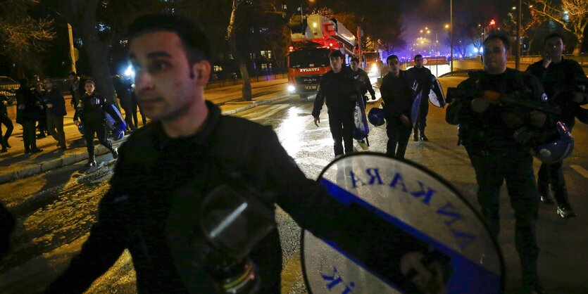 Ein Polizist breitet die Arme aus. Im Hintergrund ist ein Krankenwagen zu sehen