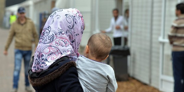 Eine Frau mit Kind auf dem Arm steht vor Wohncontainern