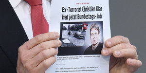 zwei Hände halten ein Blatt Papier, auf dem steht „Ex-Terrorist Christian Klar hat jetzt Bundestagsjob“