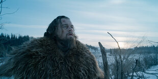 Leonardo DiCaprio steht in seiner Rolle als Hugh Glass im Film "The Revenant" auf einem freien Feld. Er trägt einen Pelzmantel