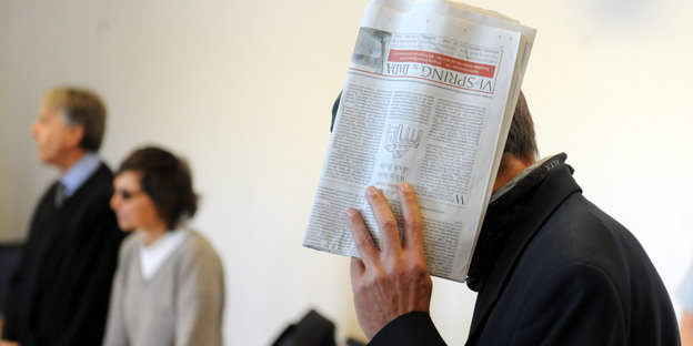 Christian Klar verdeckt sein Gesicht mit einer Zeitung