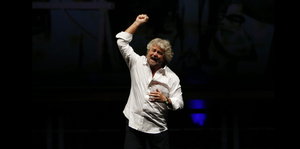 Beppe Grillo gestikuliert wild vor schwarzem Hintergrund.