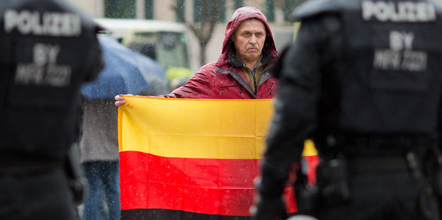 Ein Teilnehmer einer Kundgebung der Bürgerinitiative "Sichere Heimat" hält eine umgedrehte Deutschland-Flagge in den Händen