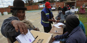 Eine Frau mit Hut steckt ihren Wahlzettel in eine Wahlbox aus Pappe.