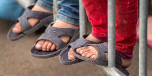 Kinderfüße in Sandalen an einem Zaun.