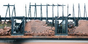 Mann steht vor einem Haus mit abgebranntem Dachstuhl.