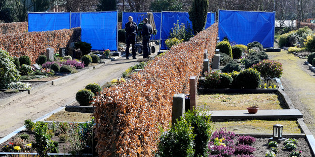 Polizisten stehen vor einem Sichtschutz auf einem Friedhof.