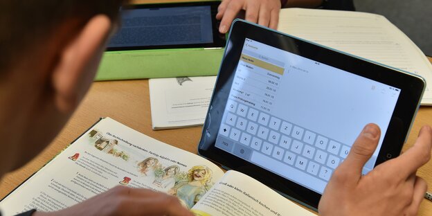 Ein Schüler arbeitet gleichzeitig mit einem Schulbuch und einem Tablet.