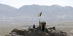 Steinbrocken mit Hütte darauf und Afghanistan-Fahne, dahinter Berge