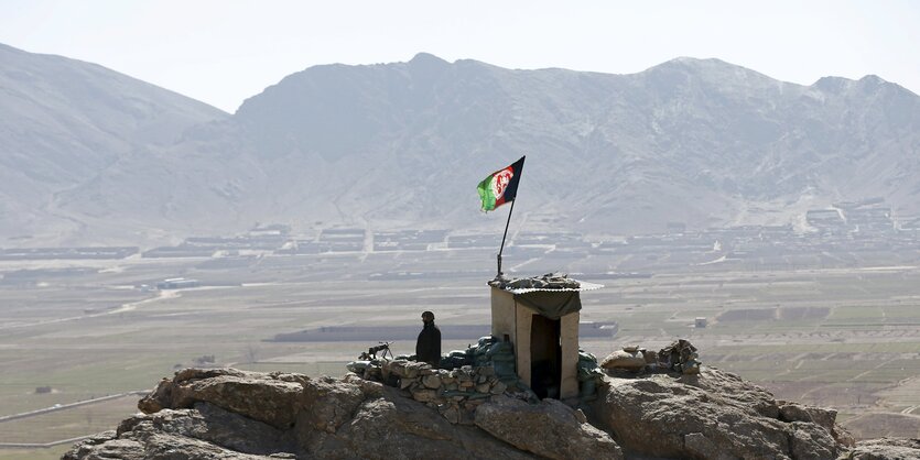 Steinbrocken mit Hütte darauf und Afghanistan-Fahne, dahinter Berge