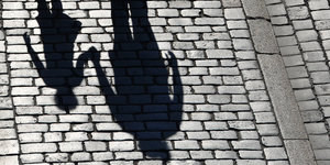 Der Schatten eines Erwachsenen, der die Hand eines Kindes hält, fällt auf Kopfsteinpflaster