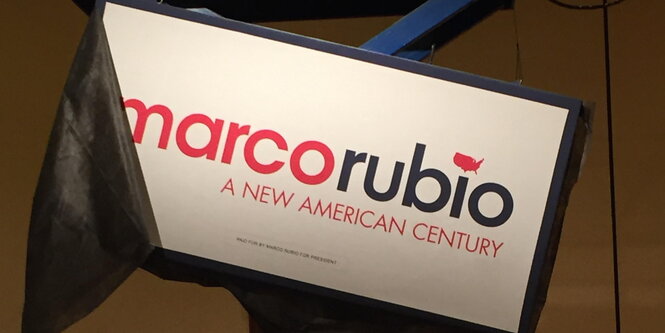 Ein Schild „Marco Rubio. A new American Century" hängt schief an einem Gestell.