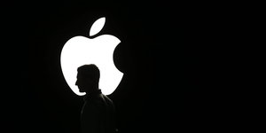 Ein weißes Apple Logo, vor dem eine Kopf zu sehen ist, vor schwarzem Hintergrund.