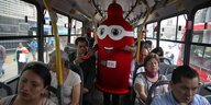 Ein Mensch in einem roten Kondomkostüm verteilt Kondome in einem Bus.