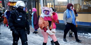 Eine Clownin begleitet einen Polizisten in Demonstrationsausrüstung durch eine Fußgängerzone.