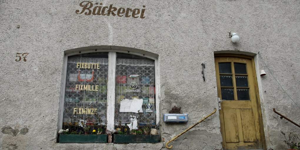 Im Fenster einer Bäckere wird für „Fixbutte, Fixmille, Fixminze“ geworben, daneben eine alte braune Eingangstür.