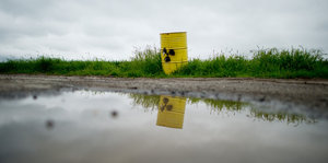 Ein gelbes Fass mit einem Atom-Zeichen steht neben einer Pfütze.