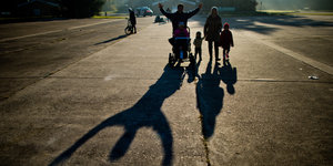 Eine Familie läuft nebeneinander im Sonnenschein. Man sieht ihre Schatten auf dem Boden