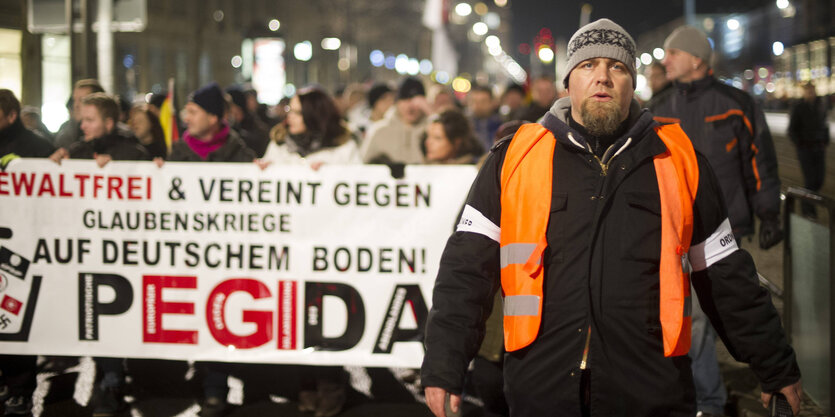 Ein korpulenter Mann läuft vor einer Pegida-Demo.