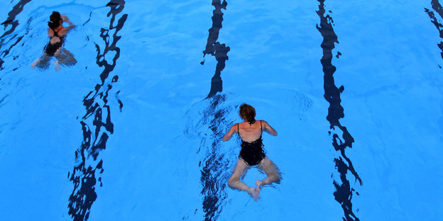 Zwei Frauen ziehen ihre Bahnen im Schwimmbad. Sie halten Abstand