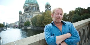 Blonder Mann steht auf Brücke in Berlin. Im Hintergrund ist die Spree zu sehen.