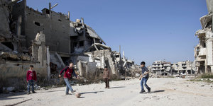 Jungen spielen zwischen Ruinen auf einer staubigen Straße Fußball