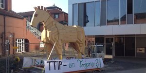 Holzpferd vor einem Bürogebäude, darunter ein Transparent mit der Aufschrift "TTIP - ein Trojaner?"