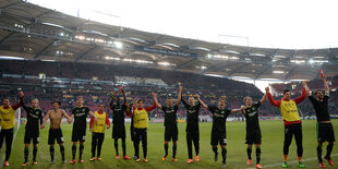 Jubelnde Spieler halten sich an den Händen, in einem Stadion