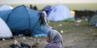 Frau mit Kopftuch vor Zelten auf Acker