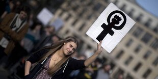 Eine junge Frau hält auf einer Demo ein Schild mit einem Venussymbol hoch.