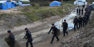Eine Reihe Polizisten läuft eine Straße zwischen Zelten entlang