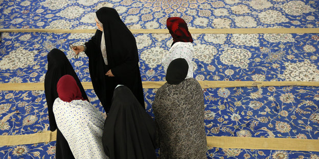 Muslima mit Kopftüchern stehen auf einem bunten Teppich.