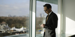 Mann im Anzug, es ist Justizminister Heiko Maas, steht mit Handy am Fenster