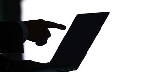 Eine Hand zeigt auf einen Laptop.