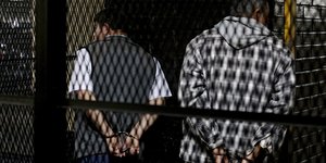zwei Männer stehen mit gefesselten Händen hinter einem Gitter